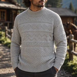 May include: A light grey long-sleeve jumper featuring a mock neck collar and a complex knit pattern. The design includes horizontal bands of textured diamond shapes, zigzag lines, and intricate cable-knit details across the chest and sleeves.