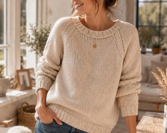 May include: A cream-colored long-sleeve knit sweater with a ribbed crew neckline, cuffs, and hem, paired with blue denim jeans. The sweater features a raglan sleeve construction with visible vertical knit detailing along the shoulder seams.