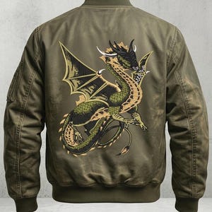 May include: Olive green bomber jacket featuring a detailed embroidered dragon design on the back. The dragon is depicted in shades of green, gold, and black, with intricate wing and scale details. The jacket has a ribbed collar, cuffs, and hem, and a pocket on the left sleeve.