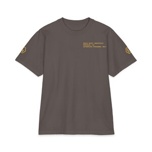Puede incluir: Una camiseta gris con mangas cortas. La camiseta tiene gráficos dorados en las mangas y el texto "AEGIS HEAVY INDUSTRIES PROTOCOL: EX AUTHORIZED PERSONNEL ONLY" en la parte superior del pecho.