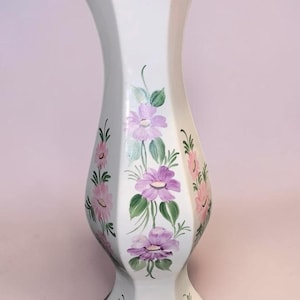 May include: White ceramic vase with a scalloped rim and a gold trim. The vase is decorated with hand-painted pink and purple flowers and green leaves. A decorative floral vase.