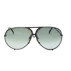 K&ouml;nnte beinhalten: Aviator-Sonnenbrille mit schwarzem Metallrahmen und gr&uuml;n get&ouml;nten Gl&auml;sern. Die Sonnenbrille hat einen Doppelsteg und eine klassische Tropfenform. Ein modisches Accessoire zum Schutz der Augen.