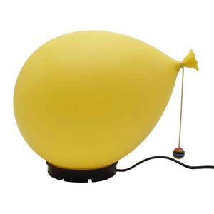 May include: A whimsical yellow balloon-shaped lamp with a black base and a small, colorful ball hanging from a string. The lamp is designed to resemble a balloon tied off at the end, with a power cord extending from the base.