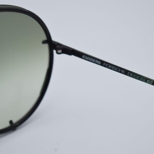 K&ouml;nnte beinhalten: Schwarze Carrera Porsche Design Sonnenbrille mit rundem Rahmen und Farbverlaufsgl&auml;sern. Der B&uuml;gel tr&auml;gt den Markennamen in gr&uuml;ner Schrift. Ein stilvolles Accessoire zum Schutz der Augen.