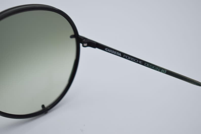 K&ouml;nnte beinhalten: Schwarze Carrera Porsche Design Sonnenbrille mit rundem Rahmen und Farbverlaufsgl&auml;sern. Der B&uuml;gel tr&auml;gt den Markennamen in gr&uuml;ner Schrift. Ein stilvolles Accessoire zum Schutz der Augen.