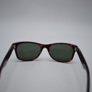 Pode incluir: &Oacute;culos de sol com um design cl&aacute;ssico. As arma&ccedil;&otilde;es apresentam um padr&atilde;o tartaruga, com lentes verdes escuras. As hastes s&atilde;o de cor preta lisa. Os &oacute;culos de sol est&atilde;o sobre um fundo branco liso.