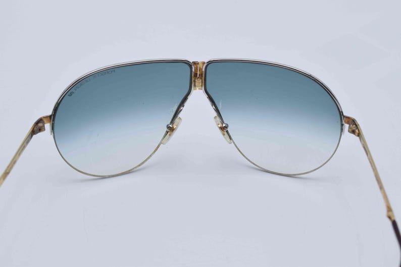 May include: Vintage aviator sunglasses with a gold-tone metal frame and gradient blue lenses. The lenses transition from a darker blue at the top to a lighter blue at the bottom. The frame has a classic double bridge design.