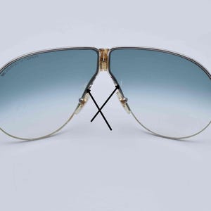 May include: Vintage aviator sunglasses with a gold-tone frame and gradient blue lenses. The lenses transition from a darker blue at the top to a lighter blue at the bottom. The frame has a classic design.