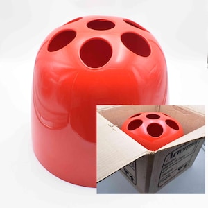 May include: A vibrant red toothbrush holder, cylindrical in shape, featuring six circular holes on its upper surface. The image also shows a similar holder inside a cardboard box. Made of plastic.