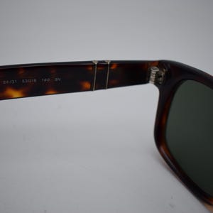 Pode incluir: &Oacute;culos de sol tartaruga com lentes escuras. A arma&ccedil;&atilde;o apresenta um design cl&aacute;ssico com uma dobradi&ccedil;a vis&iacute;vel e o texto "2953-S 24/31 53018 140 3N" impresso na haste. As lentes s&atilde;o de cor verde escuro.