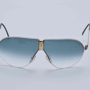 May include: Vintage aviator sunglasses with a gold frame, blue gradient lenses, and black temples. The sunglasses have a classic design with a double bridge and the brand name "Porsche Design" printed on the lens.