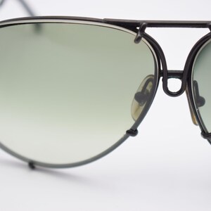 K&ouml;nnte beinhalten: Nahaufnahme einer Vintage-Pilotenbrille mit schwarzem Metallrahmen und gr&uuml;n verlaufenden Gl&auml;sern. Die Sonnenbrille hat einen Doppelsteg und Nasenpads. Die Gl&auml;ser sind oval geformt.