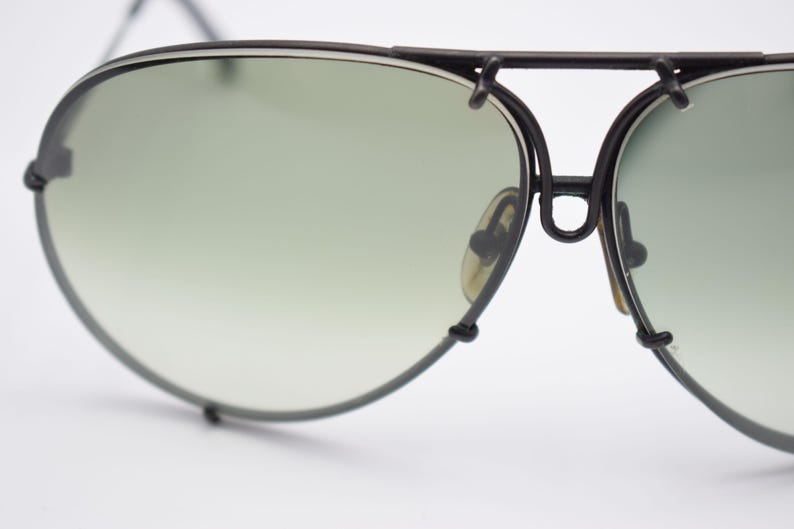 K&ouml;nnte beinhalten: Nahaufnahme einer Vintage-Pilotenbrille mit schwarzem Metallrahmen und gr&uuml;n verlaufenden Gl&auml;sern. Die Sonnenbrille hat einen Doppelsteg und Nasenpads. Die Gl&auml;ser sind oval geformt.