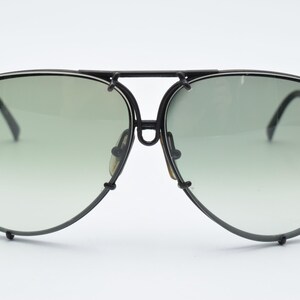 K&ouml;nnte beinhalten: Schwarze Aviator-Sonnenbrille mit gr&uuml;n verlaufenden Gl&auml;sern. Die Sonnenbrille hat einen schwarzen Rahmen und B&uuml;gel. Die Gl&auml;ser sind hellgr&uuml;n und verblassen unten zu einem helleren Farbton. Die Sonnenbrille ist ein klassischer Stil.