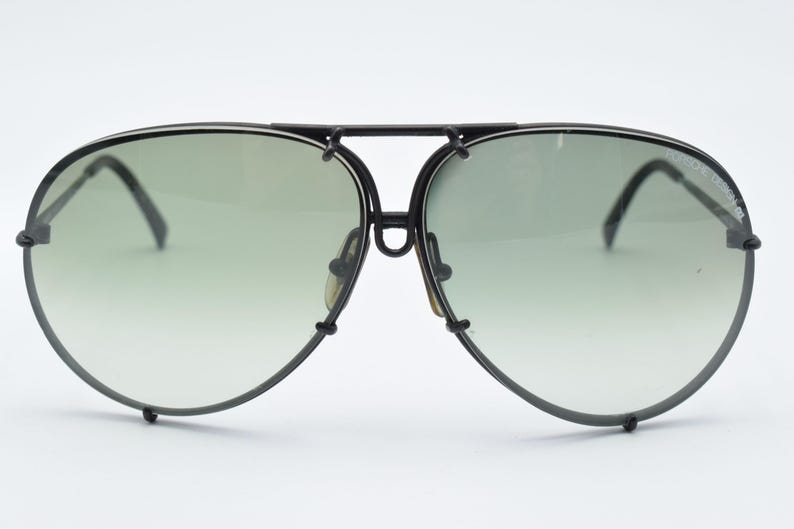 K&ouml;nnte beinhalten: Schwarze Aviator-Sonnenbrille mit gr&uuml;n verlaufenden Gl&auml;sern. Die Sonnenbrille hat einen schwarzen Rahmen und B&uuml;gel. Die Gl&auml;ser sind hellgr&uuml;n und verblassen unten zu einem helleren Farbton. Die Sonnenbrille ist ein klassischer Stil.