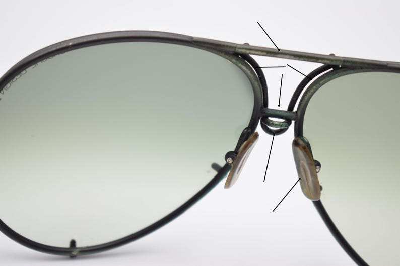 K&ouml;nnte beinhalten: Nahaufnahme einer Pilotenbrille mit dunklem Metallrahmen und Farbverlaufsgl&auml;sern. Die Nasenpads sind hellbraun. Die Sonnenbrille hat ein klassisches Design.