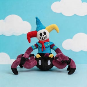 May include: A plush toy featuring a white skull head with a wide grin, wearing a blue, red, and yellow jester hat. The torso is blue with a red neck scarf, and the lower body is a black, spider-like creature with multiple purple legs.