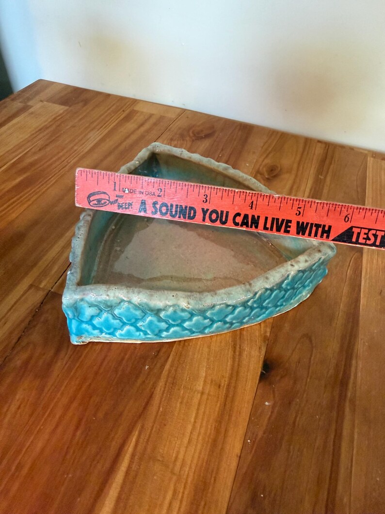 Może przedstawiać: Tr&oacute;jkątna ceramiczna miska z turkusowym zewnętrzem i jasnobrązowym wnętrzem. Miska ma około 15 cm długości. Obręcz ma teksturowany wz&oacute;r w kształcie fali. Tekst na linijce brzmi "A SOUND YOU CAN LIVE WITH".