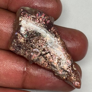 May include: A triangular-shaped sunstone gemstone featuring a polished surface with metallic copper and bronze inclusions that shimmer against a translucent, light-coloured base. The stone displays a distinct aventurescence effect with sparkling flakes.