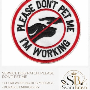 May include: A circular embroidered patch with a white background and a red border. It features a black silhouette of a dog being reached for by a hand, crossed out by a red diagonal line. The black text reads PLEASE DON'T PET ME I'M WORKING.