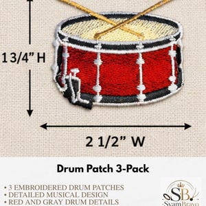 May include: A red and white embroidered drum patch with two crossed gold drumsticks. The patch measures 1 3/4 inches in height and 2 1/2 inches in width. The design features a detailed drum with black accents and a white drumhead surface.