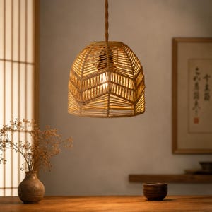 Pode incluir: Luminária pendente em rattan tecido com design geométrico. A luz, de cor bege natural, é suspensa por um cabo torcido e emite um brilho quente. A luminária tem cerca de 30 cm de diâmetro e está pendurada sobre uma mesa de madeira.
