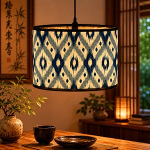 Peut inclure: Suspension cylindrique avec abat-jour à motifs. L'abat-jour présente un motif de losanges répétés en bleu marine, bleu clair et beige. La lampe est suspendue à un cordon noir, éclairant une salle à manger.
