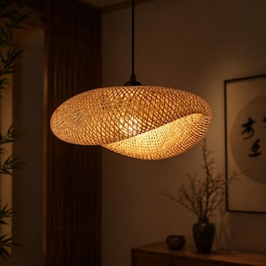 May include: A woven bamboo pendant light. The light has an organic shape, emitting a warm glow. The fixture hangs from a black cord. The natural bamboo colour complements the interior. This light is ideal for adding a touch of natural elegance to a room.