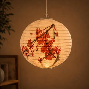 May include: A spherical paper lantern featuring a floral design. The cream-coloured lantern has a red and brown branch and flower pattern. It is suspended by a single wire and lit from within.