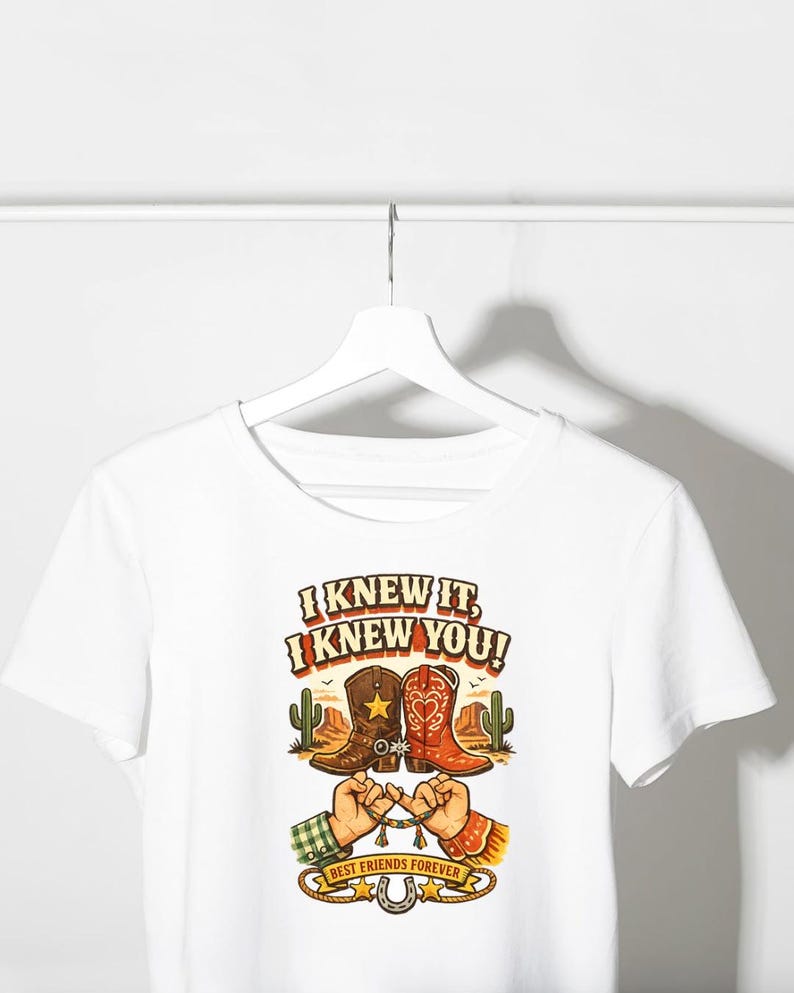 May include: A white short-sleeved t-shirt featuring a graphic print of two cowboy boots, a desert landscape with cacti, and two hands performing a pinky promise. The text reads I KNEW IT, I KNEW YOU! and BEST FRIENDS FOREVER with a horseshoe.