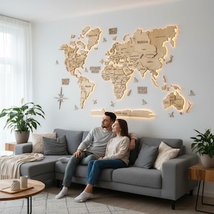 Puede incluir: Un gran mapa del mundo de madera clara como decoración de pared con nombres de países y continentes grabados. El mapa está montado en una pared blanca e incluye retroiluminación LED cálida integrada que ilumina los bordes.