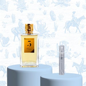 Peut inclure: Un flacon de parfum rectangulaire avec un bouchon doré et un petit flacon échantillon sur un socle bleu clair. Le flacon de parfum porte une étiquette dorée avec le chiffre 5 et le mot "Elixir". Le fond présente un motif désertique bleu clair et blanc.
