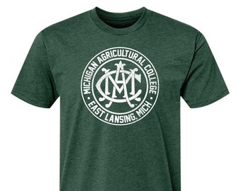 Puede incluir: Una camiseta verde con un logotipo circular blanco desgastado que dice "Michigan Agricultural College East Lansing, Mich."