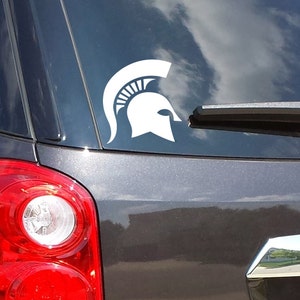 Puede incluir: Una calcoman&iacute;a de casco espartano blanco en un coche gris oscuro.