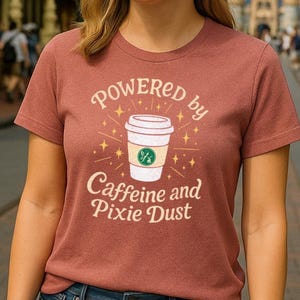 May include: A maroon t-shirt with the text "POWERED by Caffeine and Pixie Dust" in white. A cartoon coffee cup with a green logo is in the center of the text.