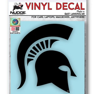 Puede incluir: Calcoman&iacute;a de vinilo negro de un casco espartano, con las palabras "VINYL DECAL" y "NUDGE. -PRINTING- Made in EAST LANSING.MI FOR CARS, LAPTOPS, MAILBOXES... ANYWHERE" arriba y "NUDGEPRINTING.COM" abajo.