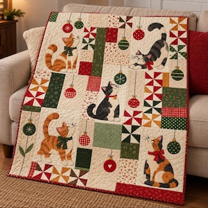 May include: A quilted throw blanket featuring a cream background with a patchwork design of red and green geometric patterns. The quilt displays five illustrated cats in various poses, accented by hanging Christmas ornament motifs.