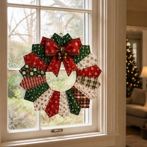 May include: A circular fabric wreath featuring alternating segments of red, green, and white patterned cotton. The design includes a large, central red bow with gold-toned accents at the top, suspended by a clear suction cup on a window pane.