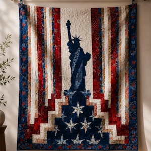 May include: A patriotic quilt featuring the Statue of Liberty in navy blue against a backdrop of red, white, and blue stripes and stars. The quilt is displayed on a wall, showcasing its handcrafted design and American theme.