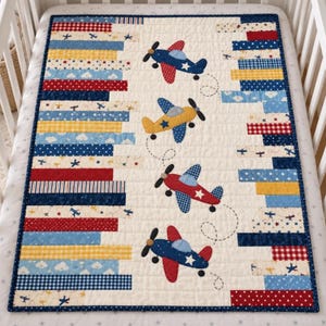 May include: A rectangular baby quilt featuring a central cream panel with four appliquéd airplanes in blue, yellow, and red. The border consists of vertical fabric strips in various patterns including gingham, polka dots, and clouds, all framed by a dark blue binding.