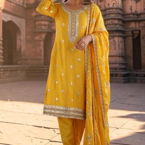 May include: A bright yellow long-sleeved tunic featuring silver sequin embroidery around the neckline, cuffs, and hem, paired with matching yellow trousers and a coordinating yellow dupatta shawl adorned with silver sequin floral patterns.