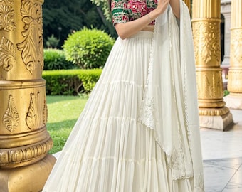 May include: A two-piece ensemble featuring a cropped blouse with a red and green floral pattern and mirror work, paired with a floor-length white tiered skirt. The skirt has a gold metallic border at the hem and includes a matching white dupatta.