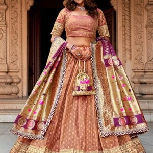 Puede incluir: Un conjunto de lehenga choli color cobre con una blusa corta y una falda voluminosa con bordados dorados. Un dupatta a juego con bordes morados y motivos de cisnes rosas se lleva sobre los brazos, junto con un pequeño bolso dorado de cordón.