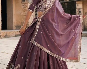 Peut inclure: Un ensemble lehenga violet profond composé d'un haut court avec des broderies dorées complexes et d'une jupe volumineuse assortie. La jupe présente une large bordure dorée ornée de sequins et de motifs floraux. Un dupatta violet transparent.