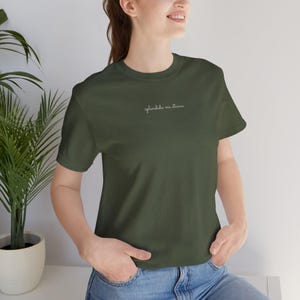 Può includere: Una t-shirt a maniche corte color verde oliva con il testo in corsivo bianco "splendida ma stanca" stampato al centro del petto. Il capo presenta un classico girocollo e un orlo dritto, offrendo un aspetto semplice e pulito.