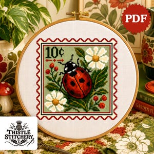 May include: A cross-stitch pattern in a wooden embroidery hoop featuring a postage stamp design with a red ladybug, white daisies, and red berries on a sage green background. The text 10c is printed in the upper left corner of the stamp design.
