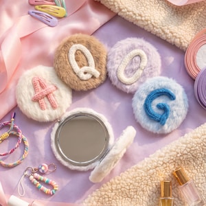 Puede incluir: Cuatro parches circulares de piel sintética con las letras tejidas A, Q, O y G en varios colores, junto a un espejo compacto de piel sintética blanca, pinzas para el cabello coloridas, un llavero de cuentas y dos frascos de perfume de vidrio.
