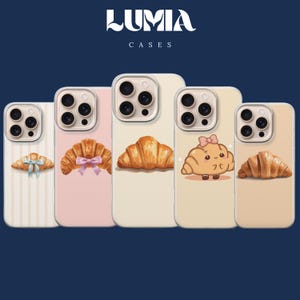 May include: Five phone cases arranged in a row, each featuring a croissant design. The cases display various styles including a croissant with a blue bow, a pink bow, a plain croissant, a cartoon croissant character, and a simple croissant.