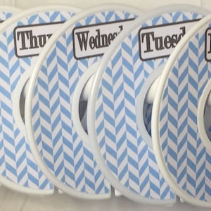 May include: Set of six white plastic hanger dividers with blue and white chevron pattern. Each divider has a black label with a day of the week written on it: Monday, Tuesday, Wednesday, Thursday, Friday, and Saturday.