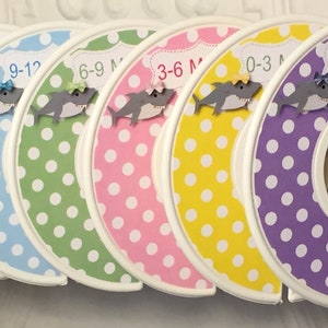 May include: Set of 8 colorful polka dot baby clothes hanger dividers with shark appliques. The dividers are labeled with sizes: Newborn, 0-3M, 3-6M, 6-9M, 9-12, 12-18, 18-24.